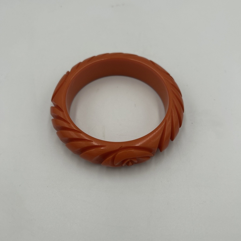 Tomato red Bakelite bangle featuring a swirl design with a floral focal point.